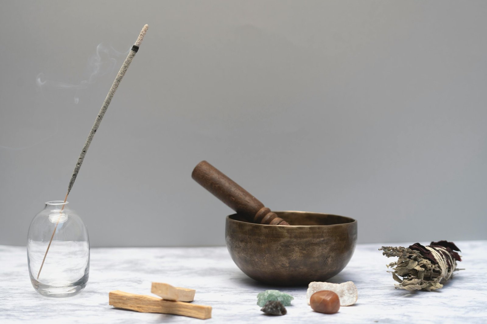 Arrangement of spiritual healing items including incense, bowl, sage, and gemstones on a marble surface.